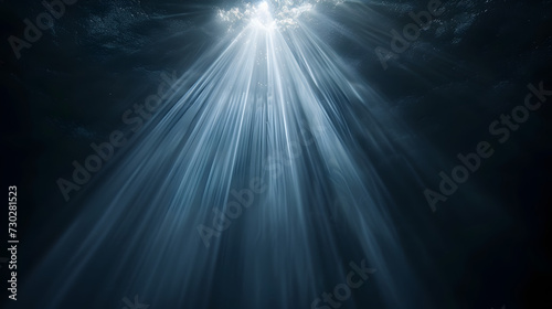 Sun rays and light shining through surface of ocean seen from underwater on black background