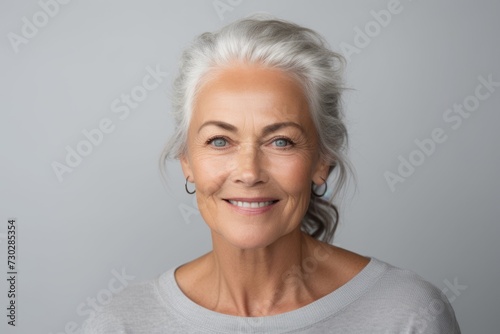 Portrait of a smiling senior woman with grey hair against grey background