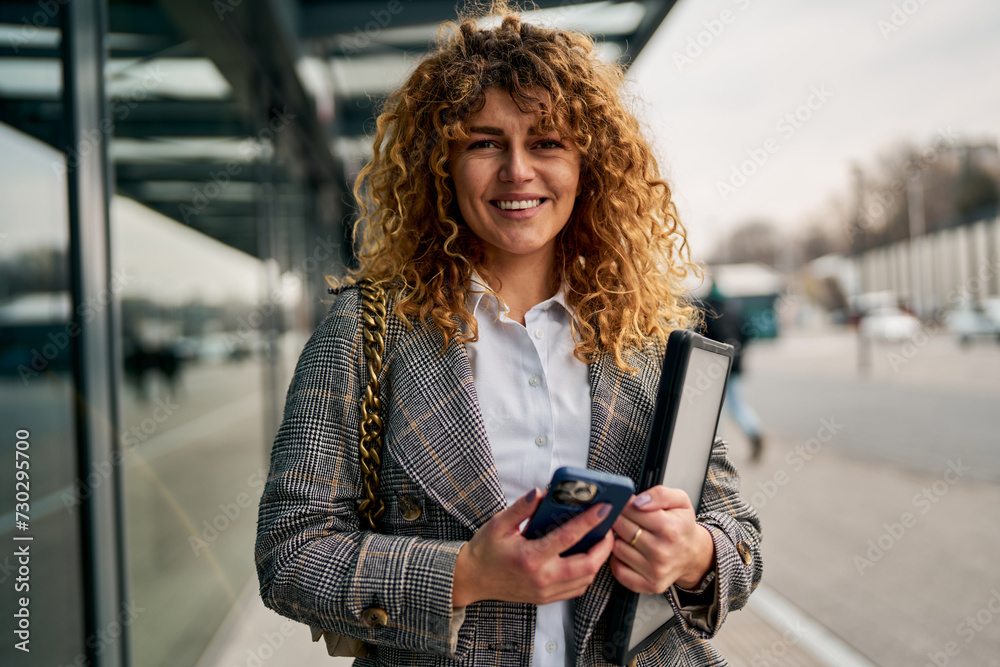 The portrait captures the essence of the confident woman, holding both phone and laptop, smiling brightly, and connecting with the camera. The portrait captures the essence of the confident woman, holding both phone and laptop, smiling brightly, and connecting with the camera.