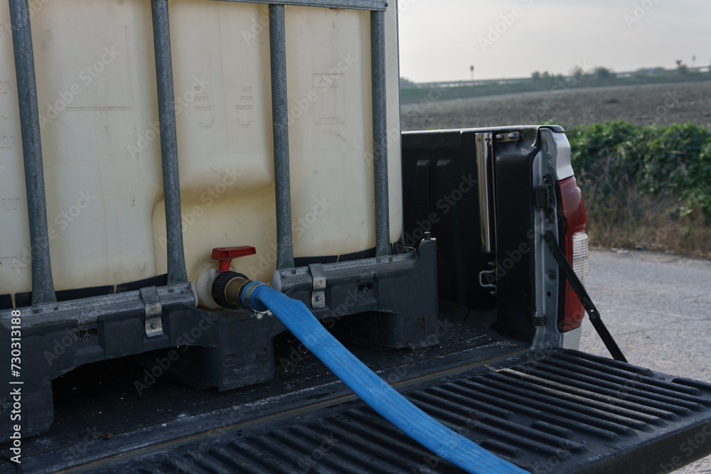 Pikup with tank, ready to fill with water. Blue hose plugged into the tank spout