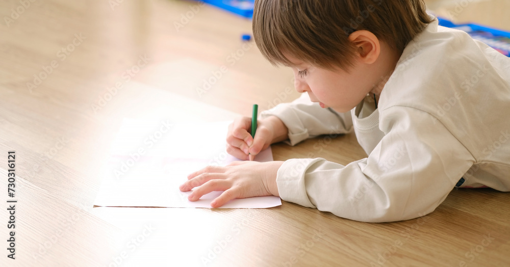 Creative child drawing with colored pencils on big white sheet, view from side Creative child drawing with colored pencils on big white sheet, view from side