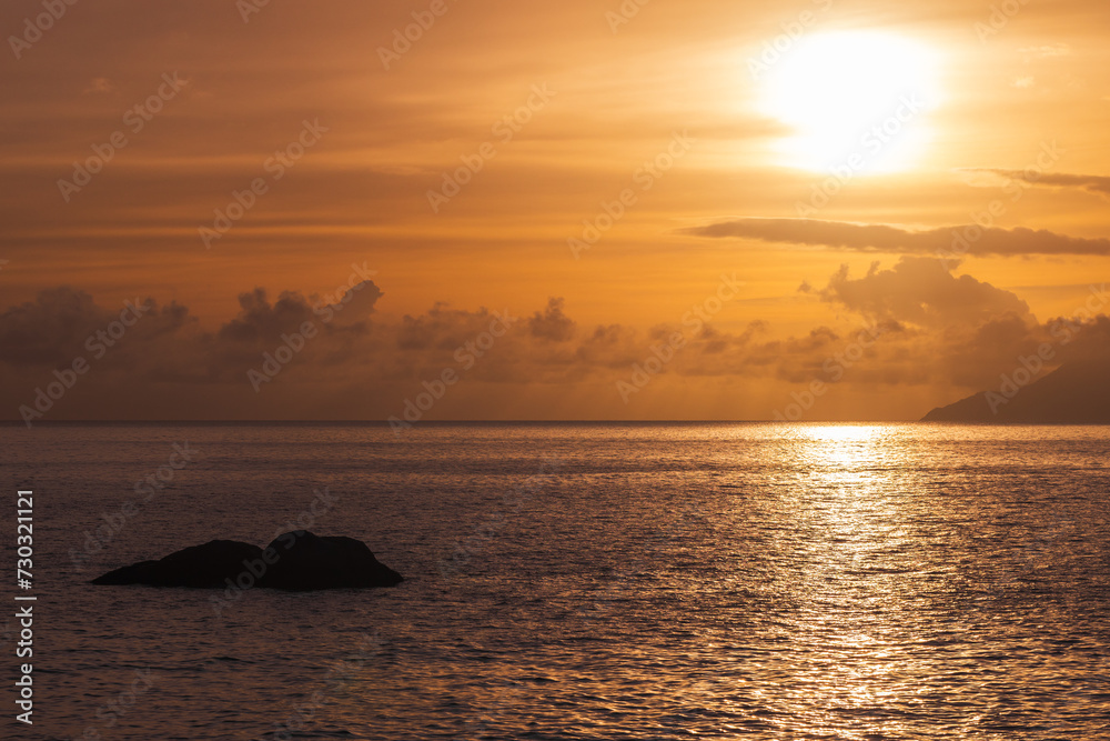 Seaside landscape, shore water and a rock under sunset sky. Seychelles