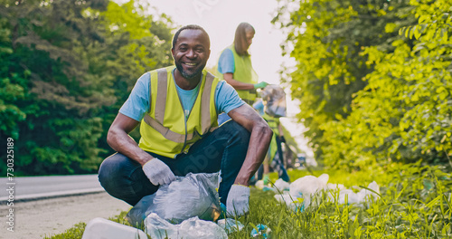 Portrait of Caring worker looking at camera with smile. African American man as part of team of enthusiastic volunteers cleaning up area near road saving nature from pollution. photo