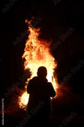 Silhouette of a person looking at big fire in the dark