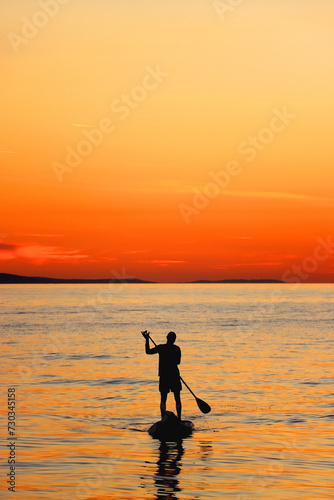 Unrecognizable person is stand up paddleboarding on the beach at sunset. Beautiful landscape in Brela, Croatia.