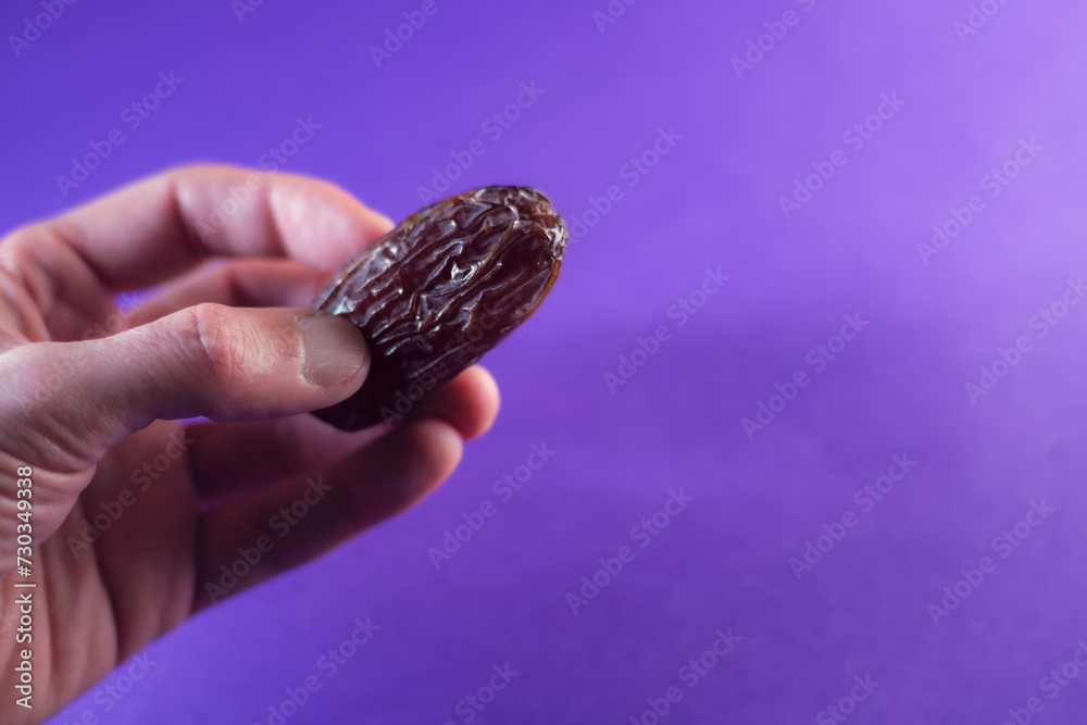 Hand with a date. A hand holds date palm on a violet background. Traditional food for iftar in Ramadan. Selective focus. Hand with a date. A hand holds date palm on a violet background. Traditional food for iftar in Ramadan. Selective focus.