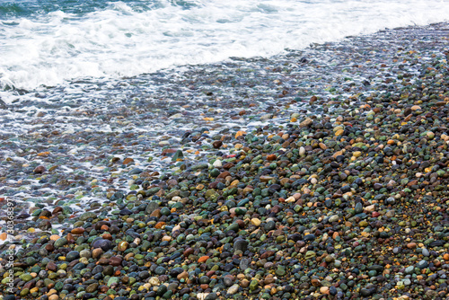 Colorful pebbles on a beach with waves approaching the shoreline © MakZin