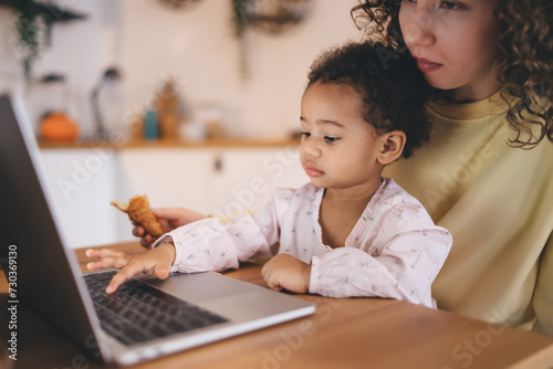 Focused ethnic daughter with mother using laptop at home