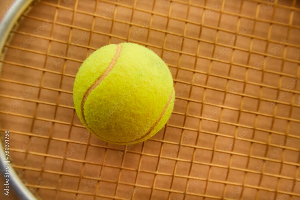 A tennis ball lies on a racket on a sandy background close-up, a ball on a racket on a clay tennis court
