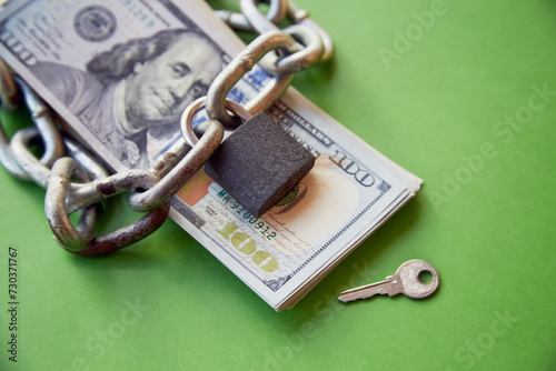 Fotografie A chain and a closed lock lay on a stack of hundred dollar bills next to the key
