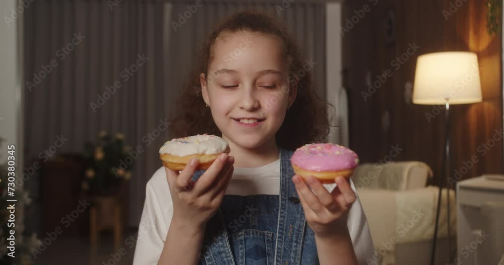 Portrait of a happy 11 year old child who can't decide whether to eat a delicious sweet dessert donut with pink glaze or white chocolate. Close-up of a caucasian child eating sweet pastries. 4K. Portrait of a happy 11 year old child who can't decide whether to eat a delicious sweet dessert donut with pink glaze or white chocolate. Close-up of a caucasian child eating sweet pastries. 4K.