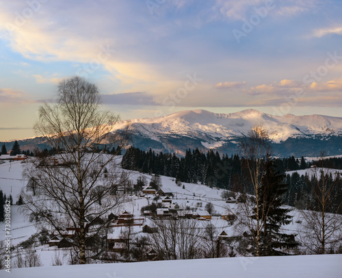 Small alpine village and winter snowy mountains in first sunrise sunlight around, Voronenko, Carpathian, Ukraine.