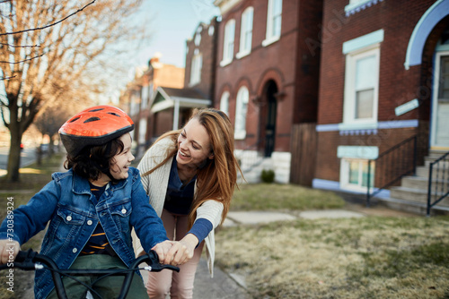 Mother helping son to learn to ride a bike outside