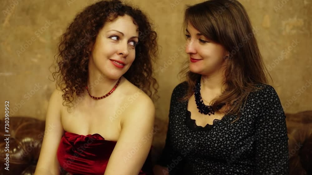 Two women sit on couch and look on each other near frayed wall Two women sit on couch and look on each other near frayed wall