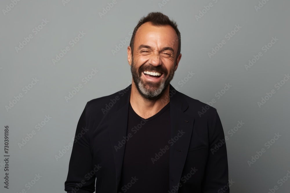Cheerful middle aged man laughing and looking at the camera while standing against grey background