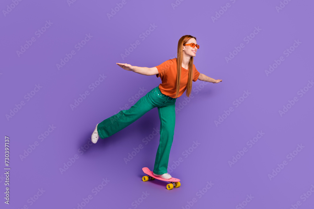 Photo of shiny sweet cheerful girl dressed stylish clothes riding penny board looking empty space isolated on purple color background