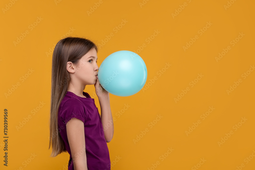 Girl inflating bright balloon on orange background, space for text Girl inflating bright balloon on orange background, space for text