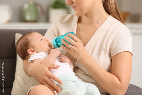 Mother feeding her cute child with infant formula indoors