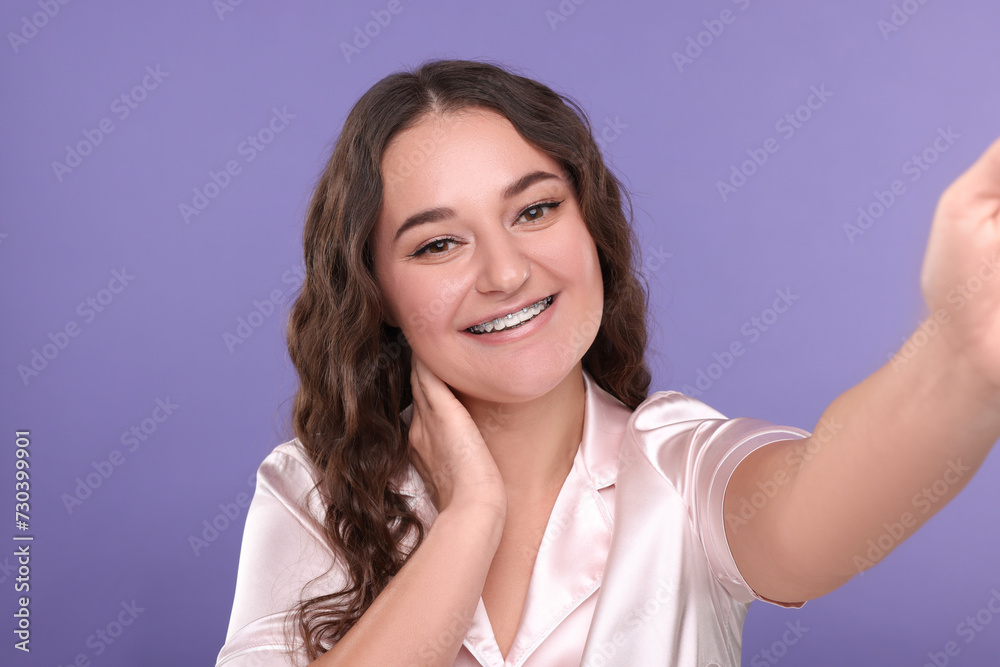 Smiling woman with braces taking selfie on violet background