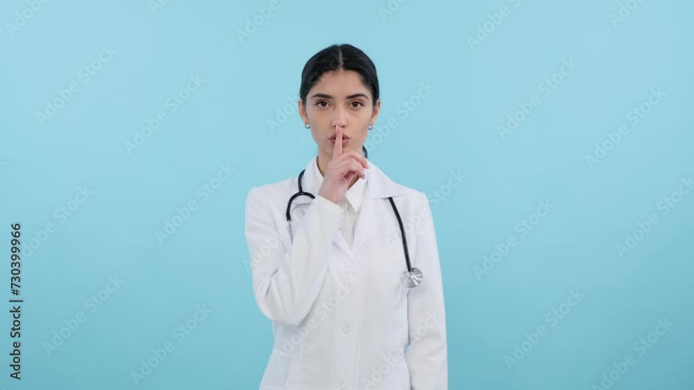 Serious Caucasian doctor or nurse showing shh gesture on blue background. Finger on lips, silence and secret gesture, ask to be quiet, secret concept. Serious Caucasian doctor or nurse showing shh gesture on blue background. Finger on lips, silence and secret gesture, ask to be quiet, secret concept.