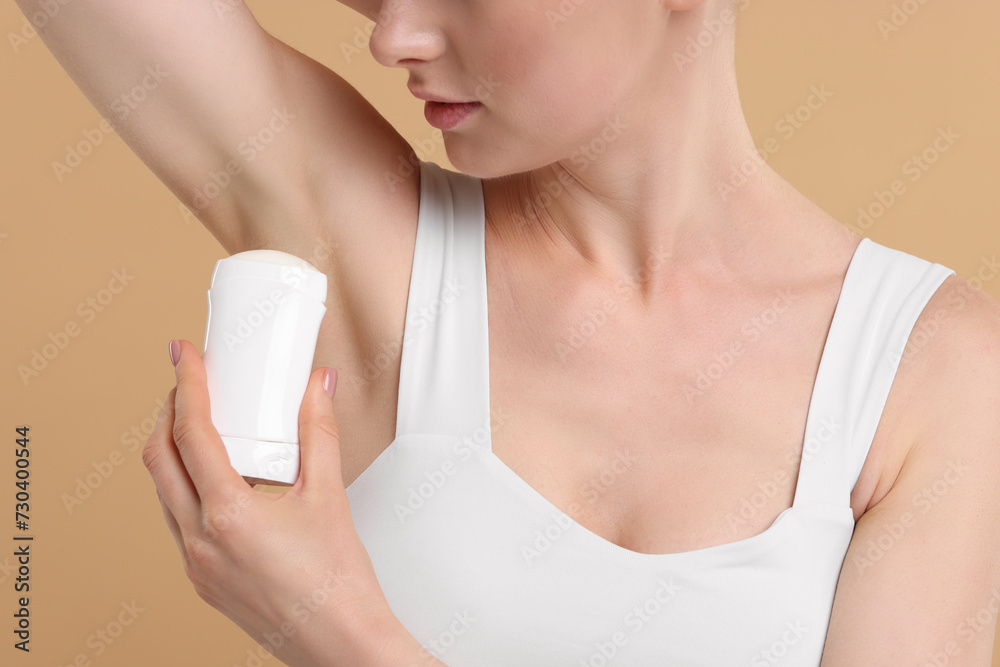 Woman applying deodorant on beige background, closeup Woman applying deodorant on beige background, closeup