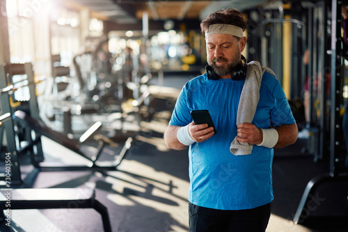 Mature athlete using app on mobile phone while exercising in gym.