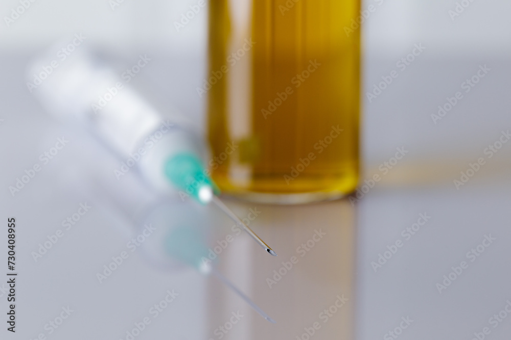 Close-up of the needle of a syringe on a white table in a laboratory or pharmaceutical clinic. Behind there is a bottle of liquid medicine out of focus. Selective focus. Blurred. Close-up of the needle of a syringe on a white table in a laboratory or pharmaceutical clinic. Behind there is a bottle of liquid medicine out of focus. Selective focus. Blurred.