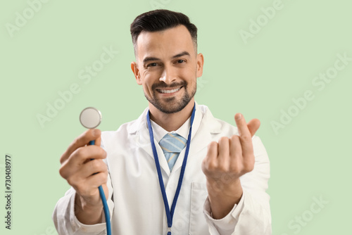 Male doctor making heart with his fingers on green background