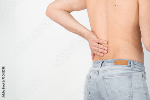 Rear view of a shirtless handsome young man holding his back in pain isolated on white background, muscular attractive man touching his lower back, back pain