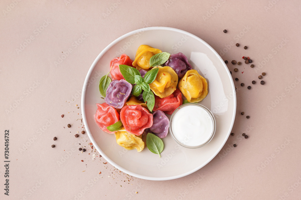 Plate of boiled colorful dumplings with basil and sour cream on beige background