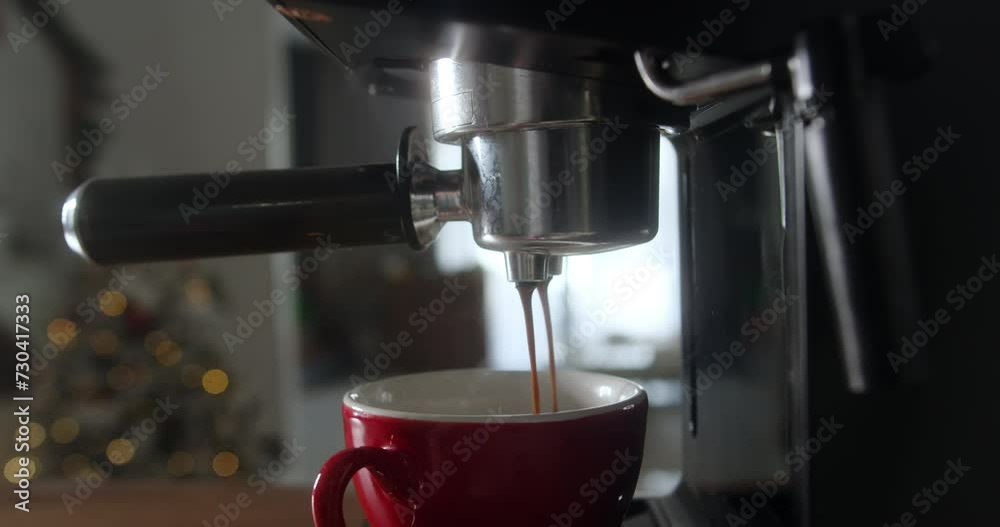 Shot roll of coffee pouring from a machine into a red cup. Homemade hot cappuccino against the backdrop of a Christmas tree and Christmas lights. Freshly ground coffee flows. Slow motion in 4K Shot roll of coffee pouring from a machine into a red cup. Homemade hot cappuccino against the backdrop of a Christmas tree and Christmas lights. Freshly ground coffee flows. Slow motion in 4K