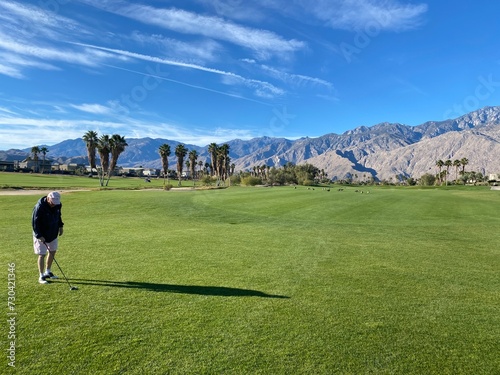 A senior man on the fairway about to hit a golf ball on a beautiful day in Palm Springs, California, USA, on a beautiful sunny winter day with the mountains in the background.