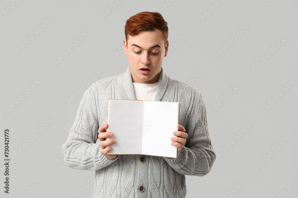 Emotional young man with blank open book on grey background Emotional young man with blank open book on grey background