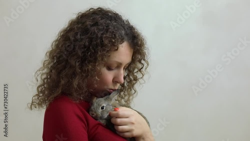 Woman pats and kisses dwarf rabbit which lies on her breast, at white background