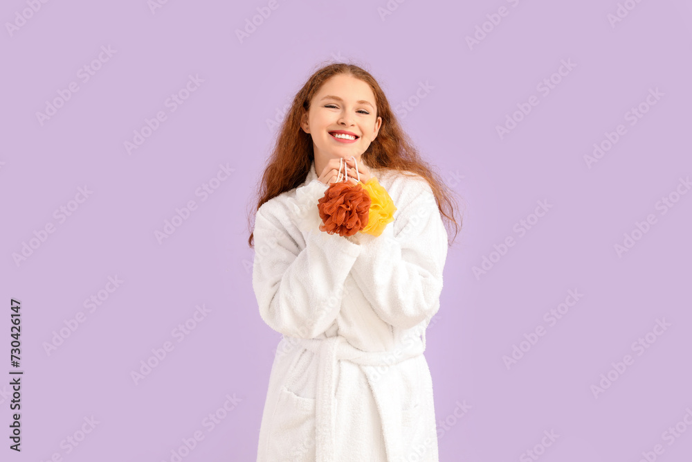 Young woman in bathrobe with loofahs on lilac background Young woman in bathrobe with loofahs on lilac background