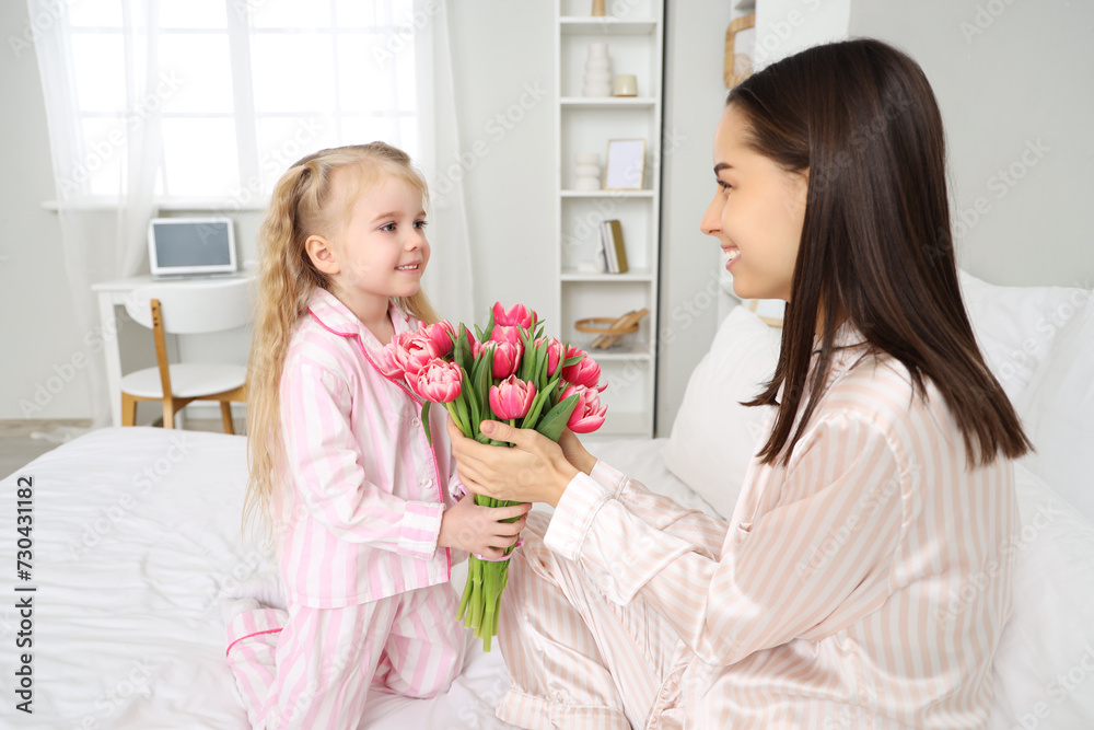 Little girl congratulating her happy mom with bouquet of beautiful flowers in bedroom. Mother's Day celebration Little girl congratulating her happy mom with bouquet of beautiful flowers in bedroom. Mother's Day celebration