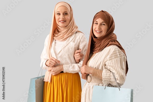 Mature Muslim women in hijabs with shopping bags on light background