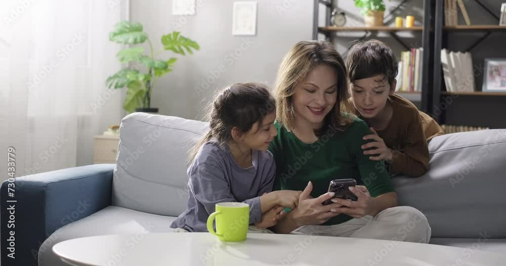 Family shopping online using smartphone, buying goods, ordering food online, sitting on couch at home. Smiling mother and children making purchase in online store