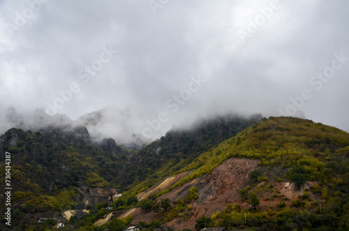 The autumn landscape from the walls of the Akhtala Monastery to the mountain slope is covered with green vegetation, the upper part of which is covered with thick fog or clouds. Lori region, Armenia