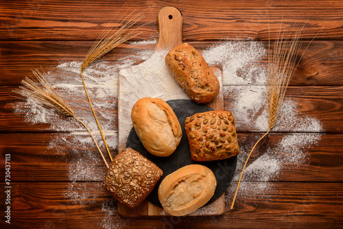 Board with fresh delicious buns, wheat ears and flour on wooden background