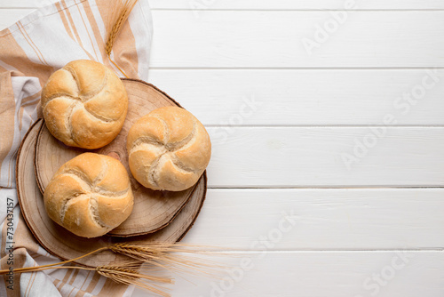 Board with delicious kaiser rolls and wheat ears on white wooden background photo