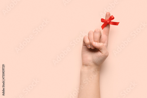 Photos Female hand with red bow on index finger against pink background