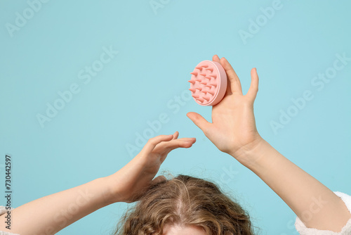 Young woman with hair scalp massager on blue background, closeup photo