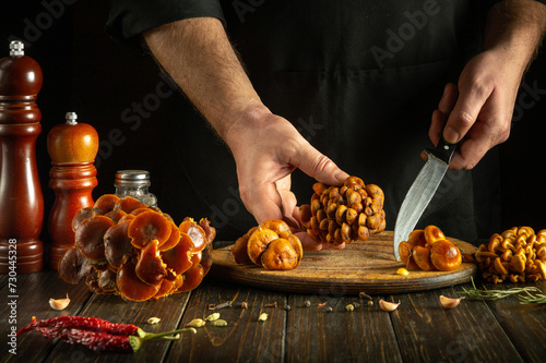 A professional chef separates fresh raw mushrooms with a knife in a hotel kitchen. Concept of preparing dietary Flammulina velutipes for lunch photo