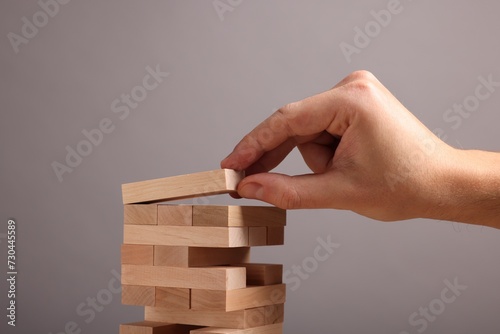 Playing Jenga. Man building tower with wooden blocks on grey background, closeup