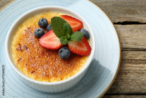 Delicious creme brulee with berries and mint in bowl on wooden table, above view