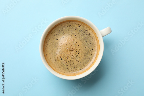 Aromatic coffee in cup on light blue background, top view