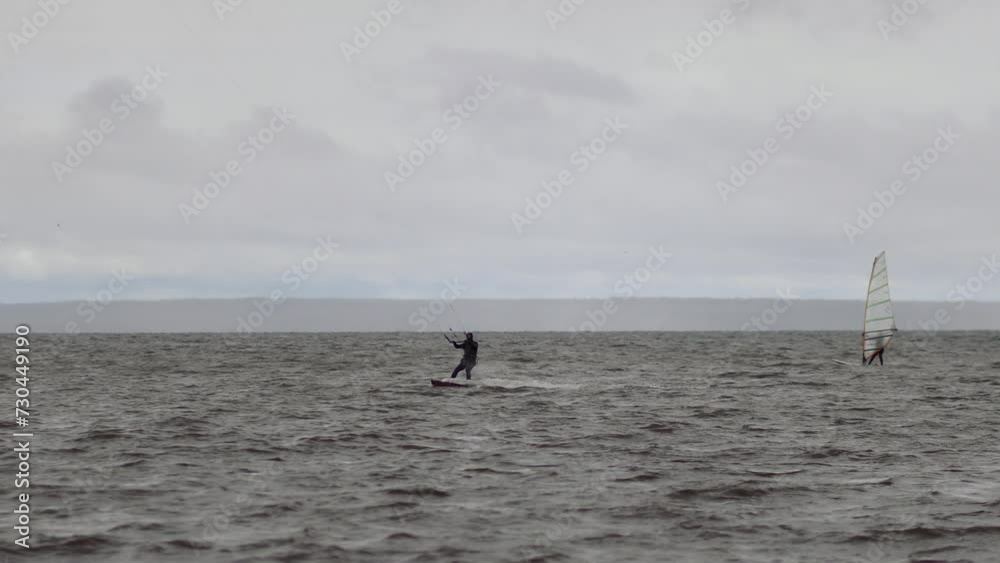 Kiteboarder moves fast by wavy water surface at cloudy day Kiteboarder moves fast by wavy water surface at cloudy day