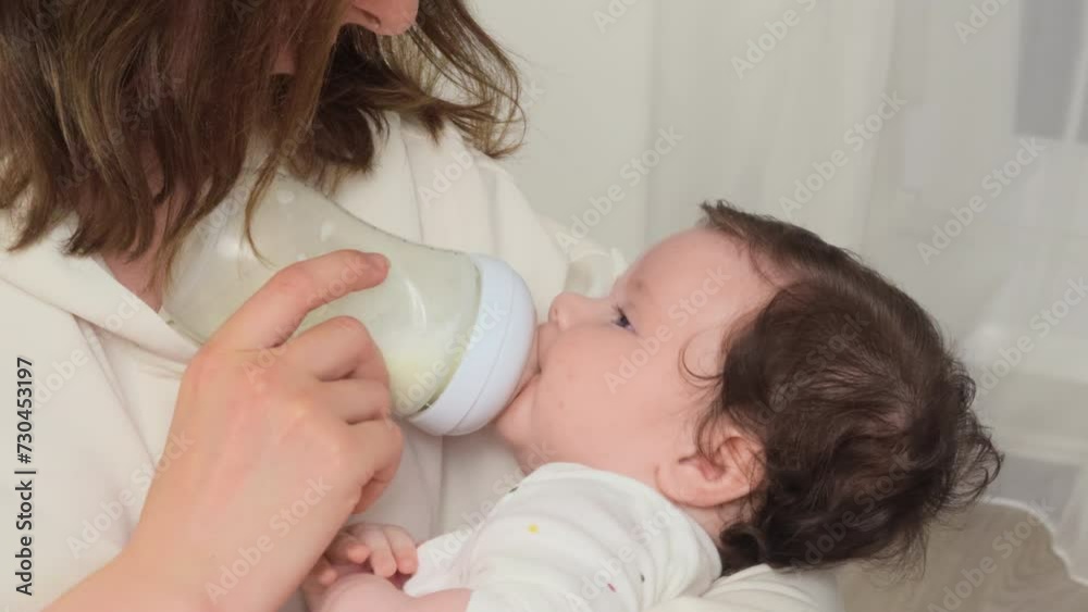 Mother gently nourishes her baby girl, using a petite baby bottle, and gazes at her daughter Mother gently nourishes her baby girl, using a petite baby bottle, and gazes at her daughter