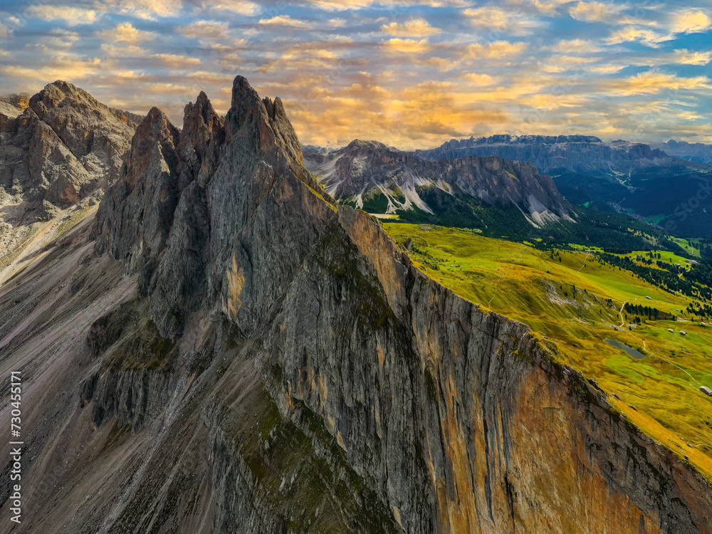 Panoramic view of high Seceda mountains and green valley at sunset.